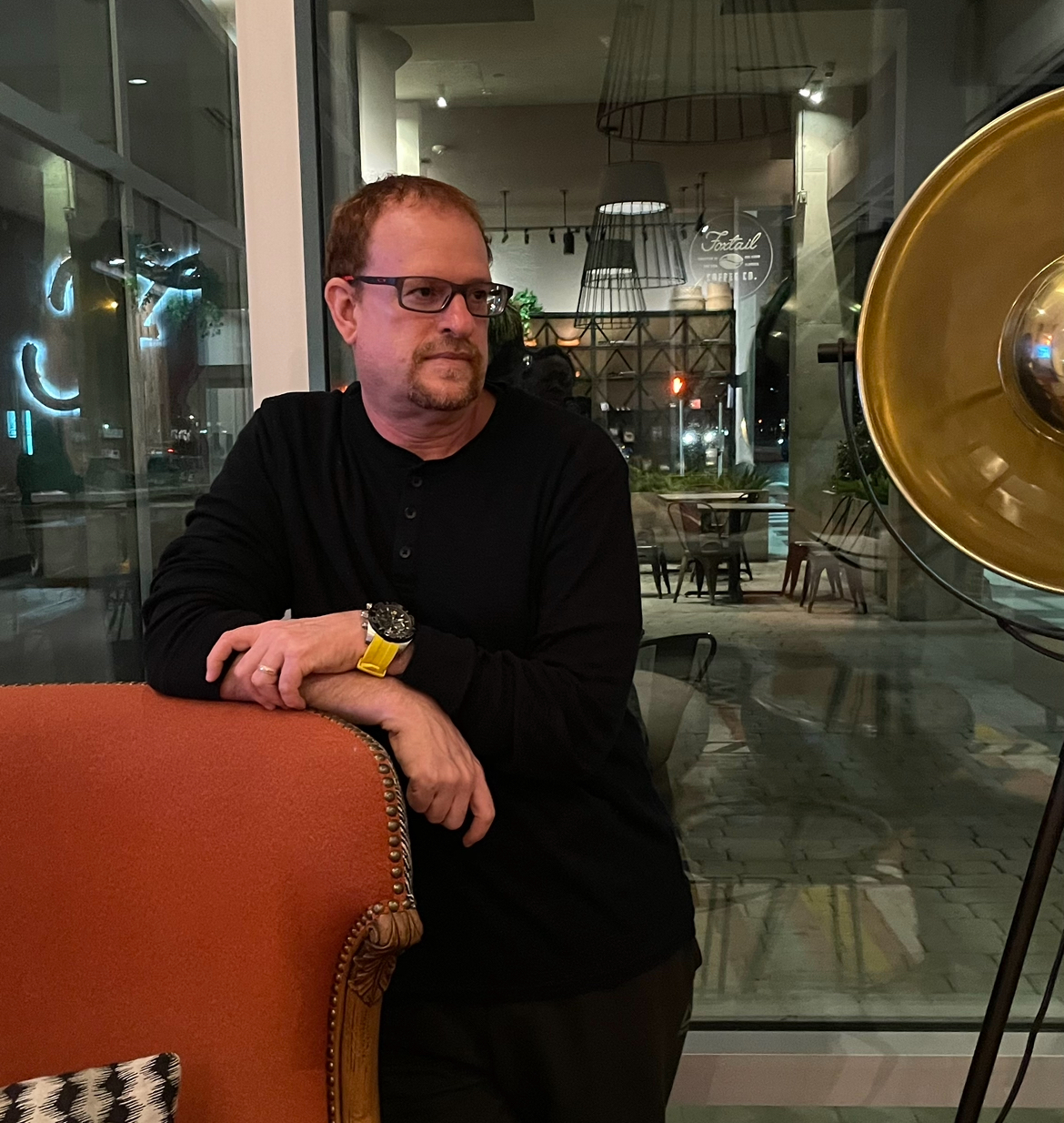 Paul Milakeve leaning on a coral armchair in a modern coffee shop at night